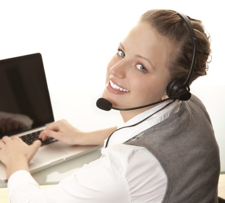 Retrato de una sonriente operadora del servicio de Atención al cliente con los cascos puestos y delante de un ordenador portátil.